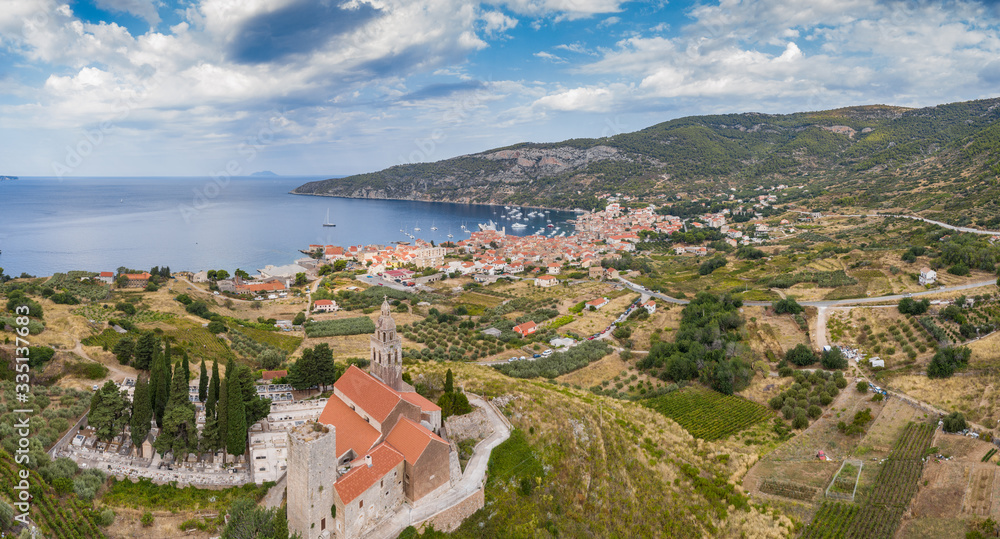 Aerial panoramic view of the cathedral St.Nicholas in Komiza city - the one of numerous port towns in Croatia, orange roofs of houses, picturisque bay, mountain is on background