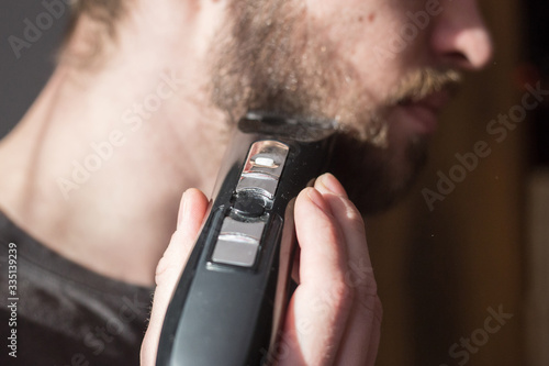 Man shaves his beard with an electric trimmer