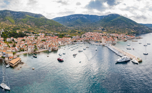 Aerial panoramic view of city Komiza - the one of numerous port towns in Croatia  is a lot of moored sailboats of a regatta  orange roofs of houses  a cathedral St.Nicholas  beach Gusarica 