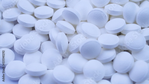 A large number of white vitamins lie nearby and rotate on the table close-up
