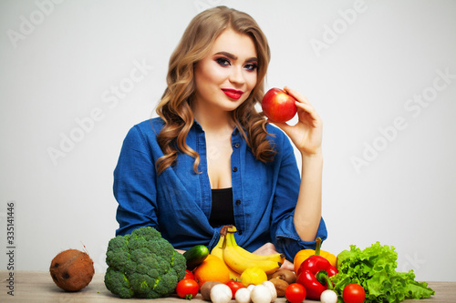 Woman with fresh vegetables and fruits on white wall background