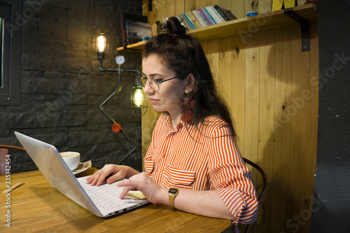Young attractive woman with glasses working with laptop in well designed home. Focused on face. Freelancer writer girl working on a project. Remote freelance work, home office concept