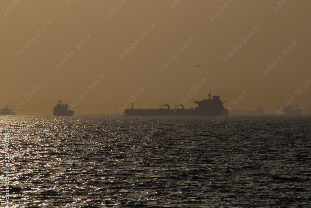 During the sunset and the golden hour on the sea, transport ships are seen.