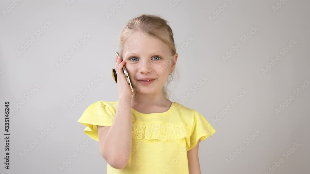 A little girl is on the phone in a bright yellow dress on a white background. Emotional conversation on the phone of a little girl. A little girl is on the phone in a bright yellow dress on a white background. Emotional conversation on the phone of a little girl.