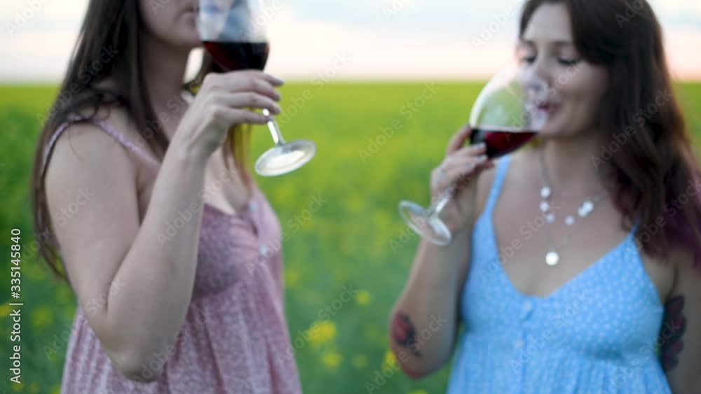 Young two women outdoors at the field drinking wine