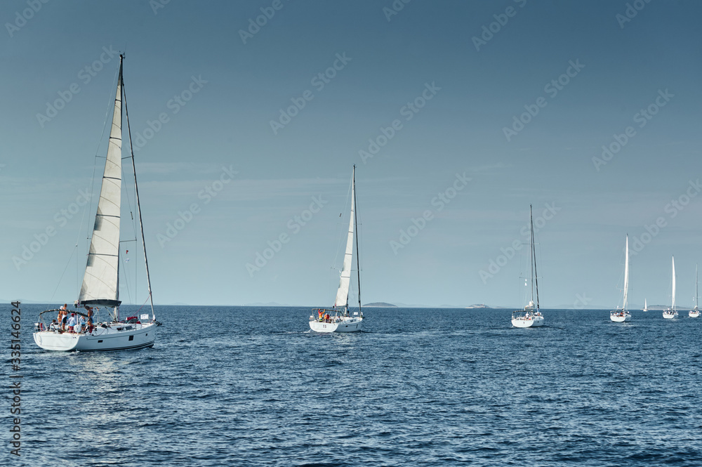 Sailboats compete in a sailing regatta at sunset, sailing race, reflection of sails on water, multi-colored spinaker, boat number aft boats, big white clouds,
