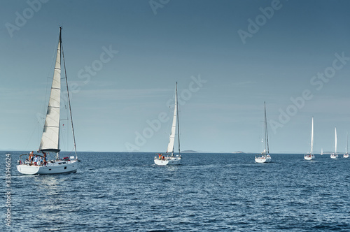 Sailboats compete in a sailing regatta at sunset, sailing race, reflection of sails on water, multi-colored spinaker, boat number aft boats, big white clouds,