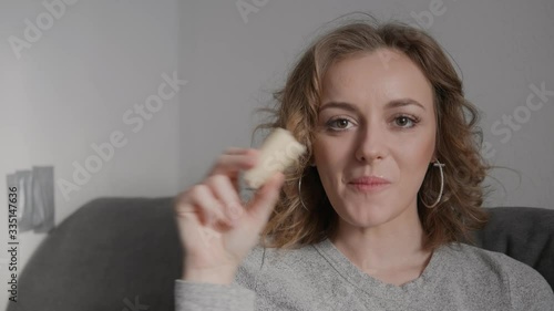 Close up shot of shy happy blonde blonde woman enjoying eating a big banana sitting on sofa white wall background smiling looking into camera