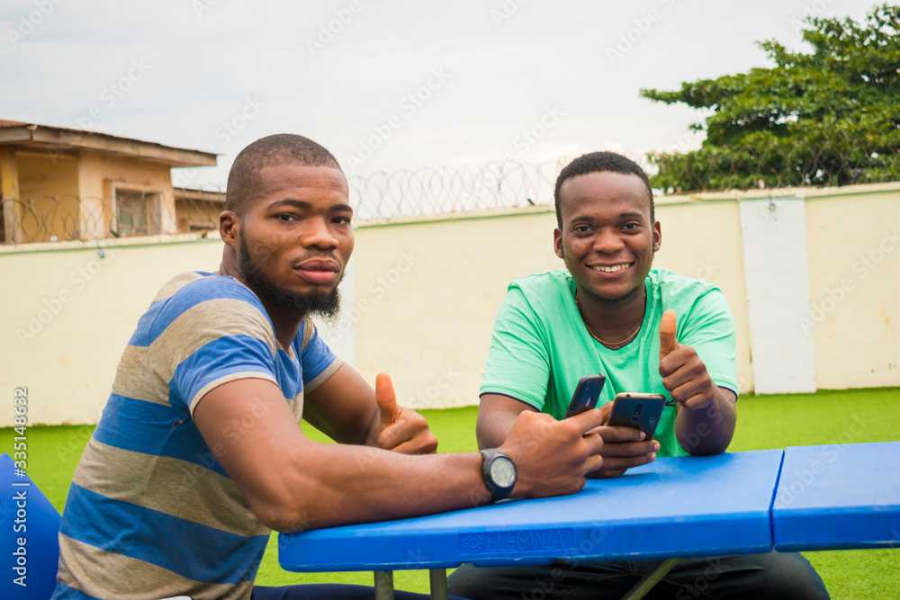 two young handsome african guys smiles as they operate their cellphone and did thumbs up