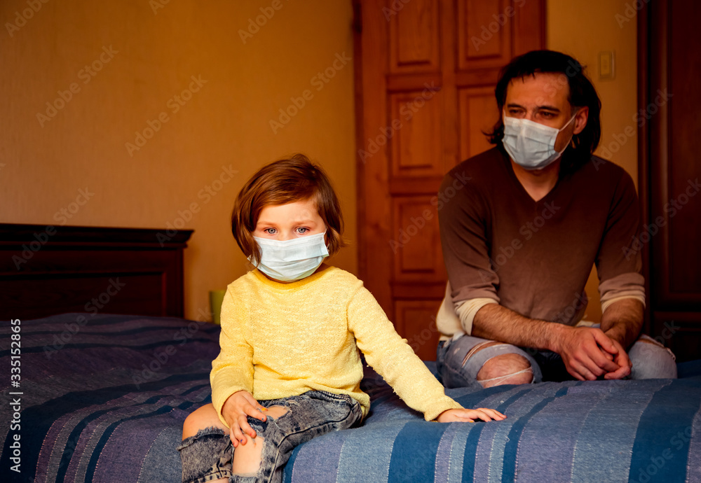 dad and daughter in a medical mask, sitting at home in quarantine, and the two of them play, because of the covid-19 pandemic