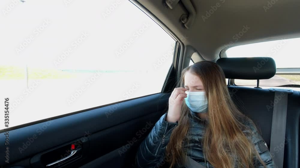 Bored sick girl in mouth mask rides in the back seat of a car and looks at the window Bored sick girl in mouth mask rides in the back seat of a car and looks at the window