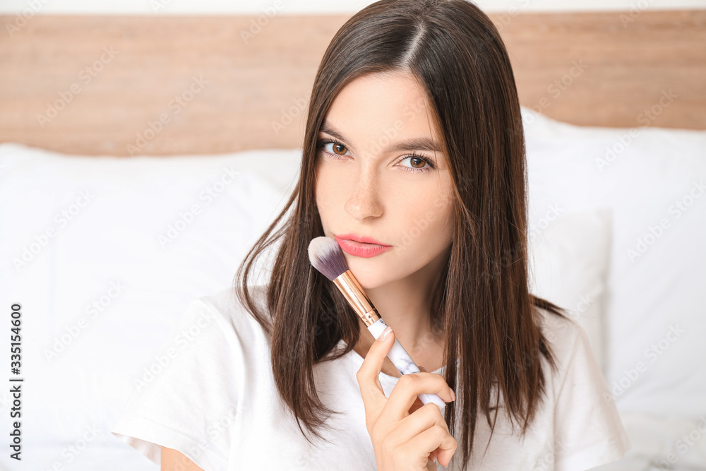 Beautiful young woman applying makeup in bedroom Beautiful young woman applying makeup in bedroom