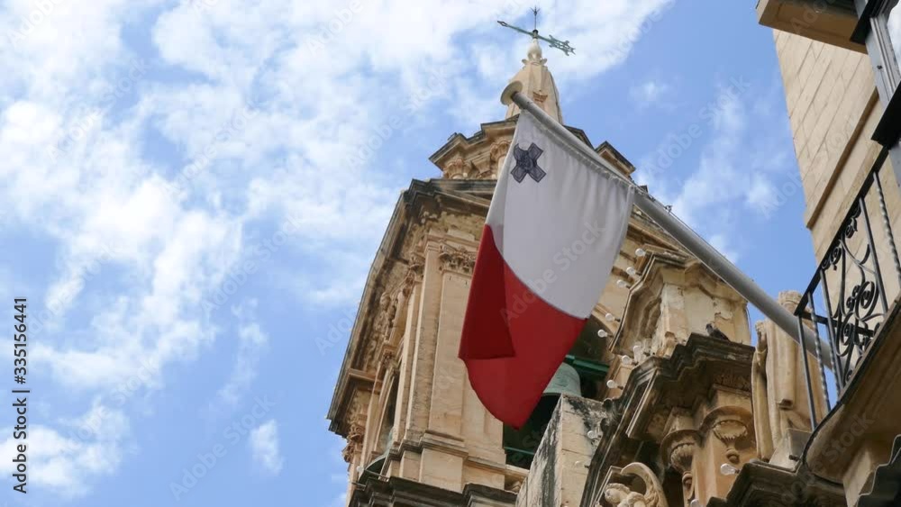 National flag of Malta waving in wind from the balcony of a building with clear blue sky in background National flag of Malta waving in wind from the balcony of a building with clear blue sky in background