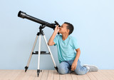 Little African-American boy with telescope near color wall