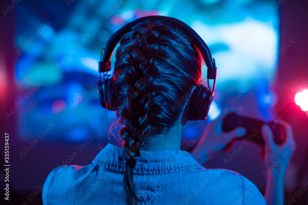 Girl in headphones plays a video game on the big TV screen. Gamer with a  joystick.