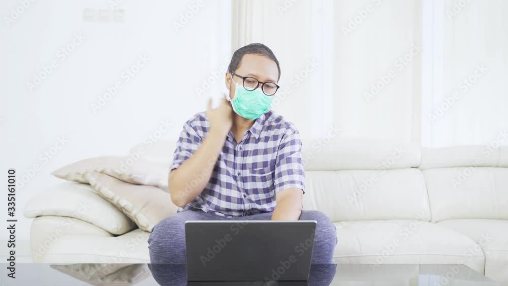 Young man working with laptop and mask while checking his fever or body temperature. Shot in 4k resolution Young man working with laptop and mask while checking his fever or body temperature. Shot in 4k resolution