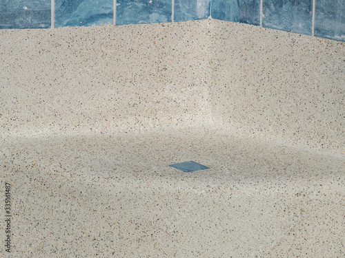 Curved seat in an empty swimming pool that is newly refinished  with cement containing small pebbles .