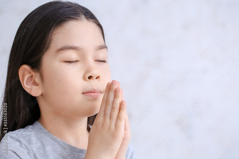Cute little Asian girl praying on light background Cute little Asian girl praying on light background
