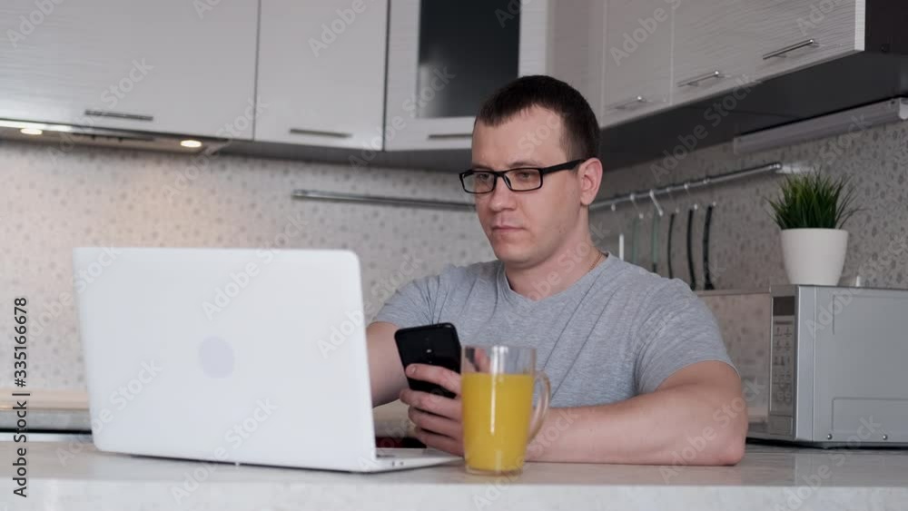 A man during remote work from home writes data from a phone to a laptop while sitting at a table. A man during remote work from home writes data from a phone to a laptop while sitting at a table.