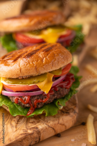 Grilled hot cheeseburger on a wood cutting board. Homemade burger with beef, cheese, vegetables, crispy buns and salt fries on a rustic table. Restaurant menu. Vertical picture, front view, close up