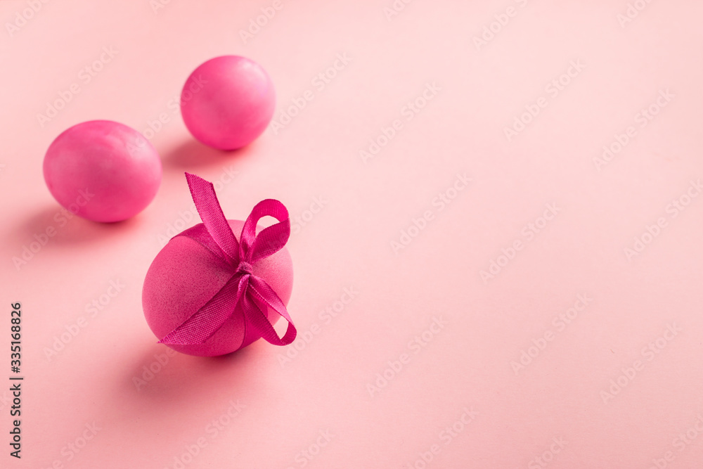 Fototapeta premium Bright pink eggs with satin bow on a pink background. Festive spring concept. Color trend.