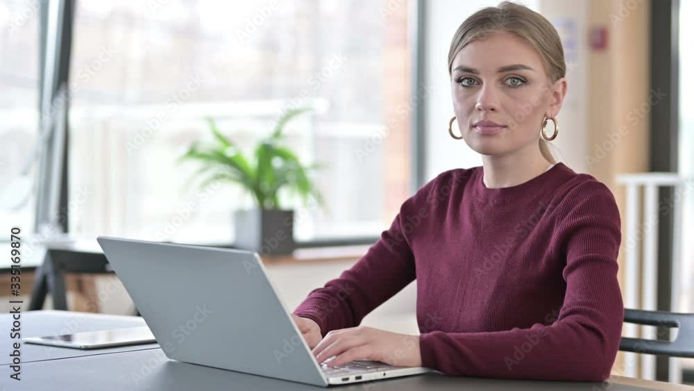 Young Woman with Laptop Looking at Camera in Office Young Woman with Laptop Looking at Camera in Office