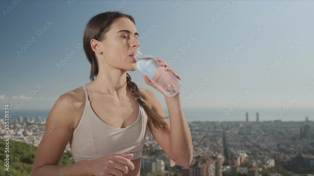 Woman opening bottle at viewpoint of city. Girl drinking water after training Woman opening bottle at viewpoint of city. Girl drinking water after training