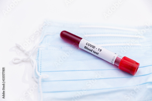 Vacuum tube with blood test identified by the COVID-19 coronavirus on white background. Protective medical mask and a tube