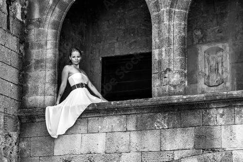 A girl in a white dress sits on a balcony with columns © Kooper