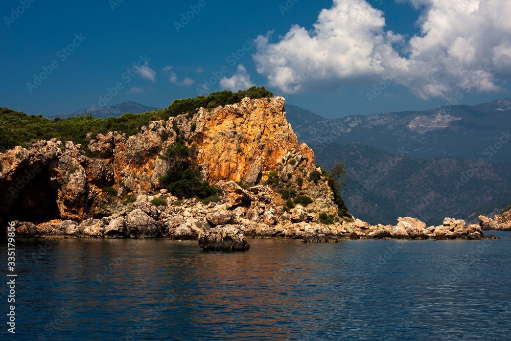 Rock in the sea, coast, mountains and sky with clouds