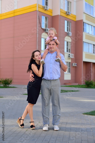 Happy family is standing near their modern house, smiling and looking at camera.