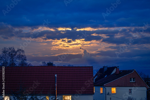 Mond hinter Wolken, warm orange leuchtend, blaue Wolken mit Häuseren mit leuchtenden Fenstern im Vordergrund, Freiraum oben