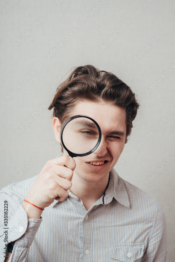 young man looking through a magnifying glass young man looking through a magnifying glass
