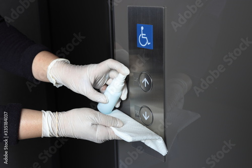 Cleaning staff cleaned the switch button of elevator with alcohol spray and wipe out with cleaned paper. Protection infected corona virus from touch public object. 