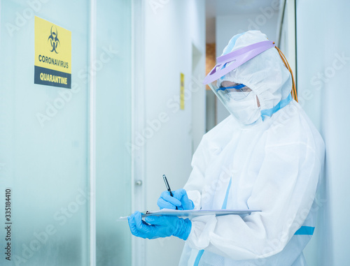 Asian doctor in personal protective suit wearing surgical mask and writing on quarantine patient chart, work hard without depression in covid-19 crisis. Medical and coronavirus concept.