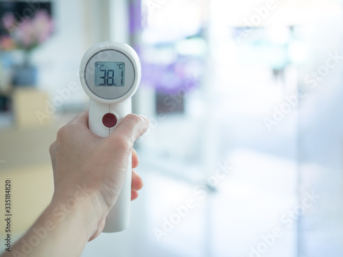 Woman holding medical infrared forehead thermometer to check body temperature, showing high fever. Initial screening to prevent coronavirus outbreak. Covid-19 and coronavirus concept.