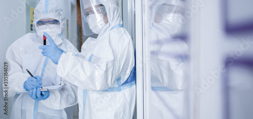 Asian woman doctor in personal protective suit with mask writing on quarantine patient chart, holding test tube with blood sample for screening coronavirus. Coronavirus, covid-19 concept.