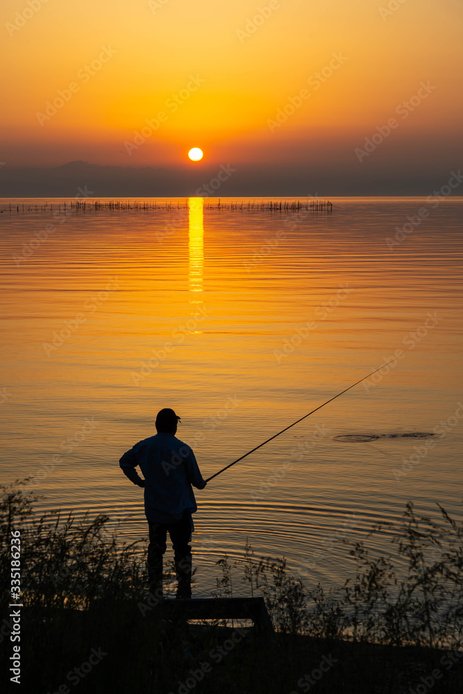 琵琶湖から昇る太陽と釣りをする人
