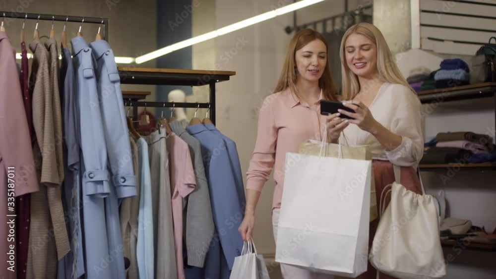 Handheld shot of happy woman and her mother holding shopping bags and taking selfie at boutique Handheld shot of happy woman and her mother holding shopping bags and taking selfie at boutique