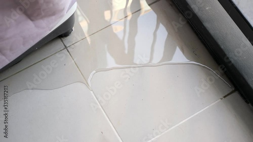trembling water puddle after pipe burst covers white tile near furniture in room reflecting window and blue sky close view
