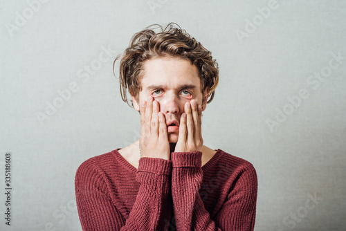 Closeup portrait, headshot young tired, fatigued business man worried, stressed, dragging face down with hands, isolated , grey background. Negative human emotions, facial expressions, feelings