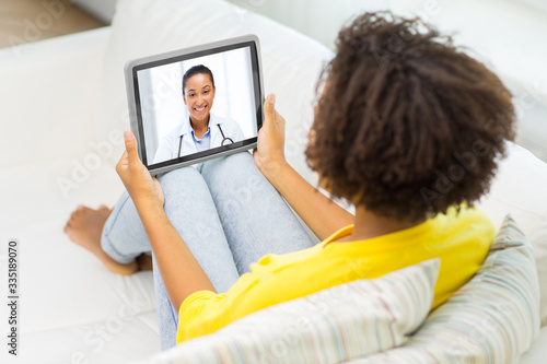 medicine, technology and healthcare concept - african young female patient having video chat with doctor on tablet pc computer at home