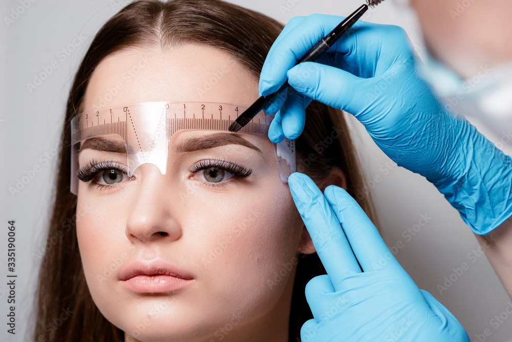 Microblading eyebrows work flow in a beauty salon. Woman having her eye brows tinted. Semi-permanent makeup for eyebrows. Focus on model's face and eyebrow