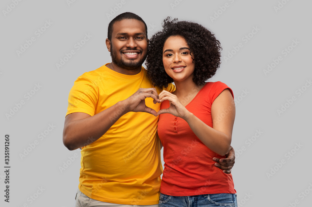 Naklejka premium love, valentines day and people concept - happy african american couple making hand heart gesture over grey background