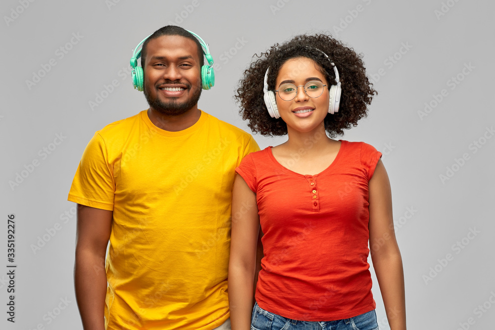 Obraz premium leisure, music and people concept - happy smiling african american couple with headphones over grey background