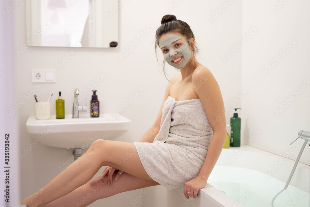 Naklejka premium Woman with clay mask taking selfie with mobile phone at home enjoying relaxation. Beautiful lady doing skincare treatment and taking selfie.Self quarantine & social distancing at home concept.