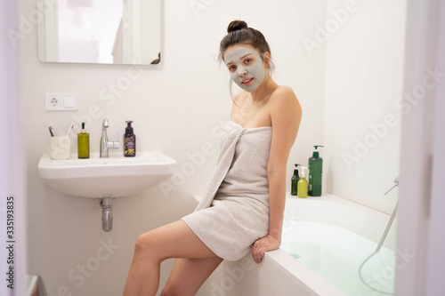 Woman with clay mask taking selfie with mobile phone at home enjoying relaxation. Beautiful lady doing skincare treatment and taking selfie.Self quarantine & social distancing at home concept.