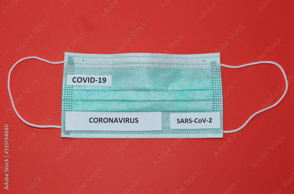 Surgical protective face mask with name of illness CORONAVIRUS, covid-19 and SARS-CoV-2 on it top view close up on red background Surgical protective face mask with name of illness CORONAVIRUS, covid-19 and SARS-CoV-2 on it top view close up on red background