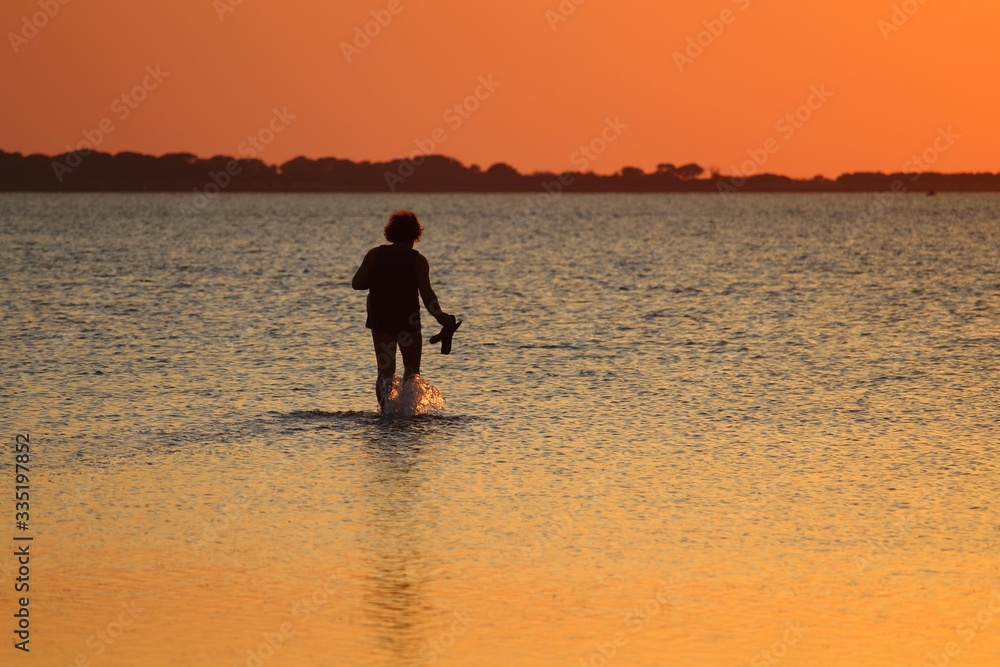 silhouette of person in backlight walking into the sea at low tide at sunset