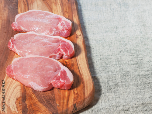 Three raw uncooked pork chops on a wooden cutting board,